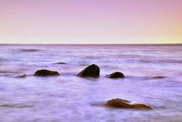 Romantic morning at sea. Big boulders sticking out from smooth wavy sea. Long exposure