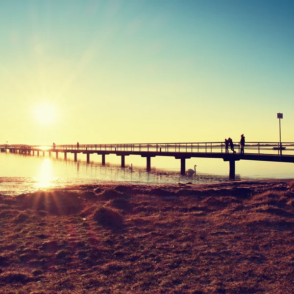 Morning in harbor. Tourists walk on pier above sea. Clear blue sky, smooth water level