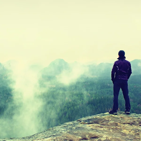 Hiker on sharp cliff of sandstone rock in rock empires park and watching over misty and foggy spring valley