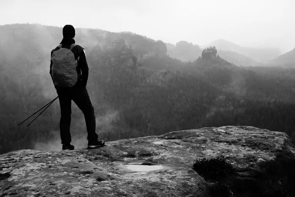 Hiker with red backpack on sharp sandstone rock in rock empires park and watching over the misty and foggy spring valley