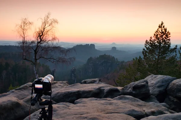 Tripod with big camera stand on mountain peak after sunset. Sharp sandstone cliffs