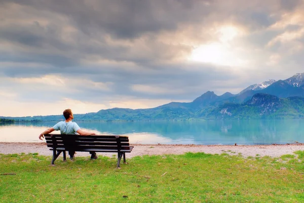 Alone  man sits on bench beside an azure mountain lake. Man relax