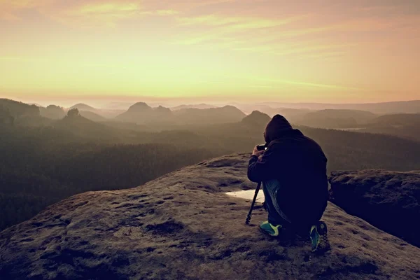 Professional on cliff. Nature photographer takes photos with mirror camera on peak of rock.