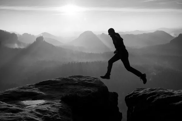 Young crazy man jump on mountain peak. Silhouette of jumping man and beautiful sunset sky. Vintage effect, lens defect.