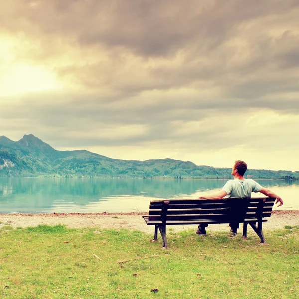 Alone  man sits on bench beside an azure mountain lake. Man relax