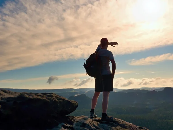 Alone tourist with sporty backpack stand on cliff edge and watching into deep valley bellow.