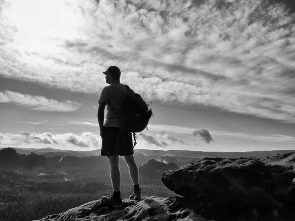 Alone tourist with sporty backpack stand on cliff edge and watching into deep valley bellow.