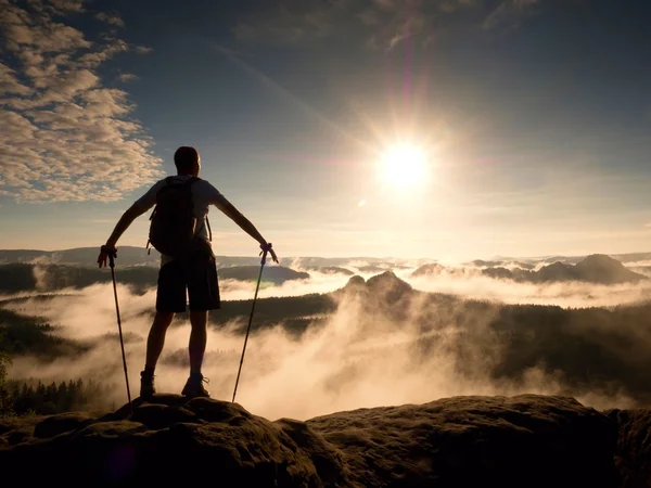 Hiker with sporty backpack on rocky view point above misty valley. Sunny daybreak