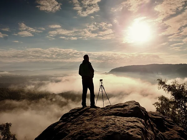 Professional photographer with tripod on cliff and thinking. Dreamy fog