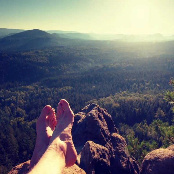 Naked male hairy legs take a rest on peak of rock. Outdoor activities in summer weather. Long forest valley in hilly landscae of nature park.