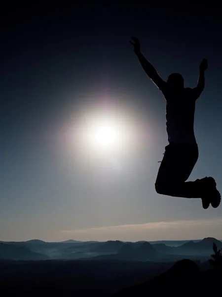 Young crazy man is jumping on rock. Silhouette of jumping man