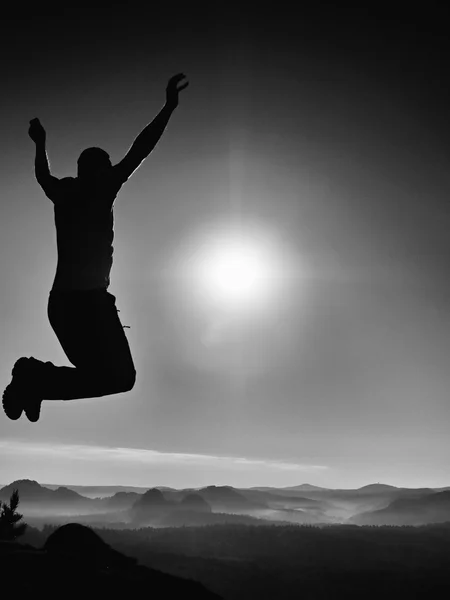 Young crazy man is jumping on rock. Silhouette of jumping man