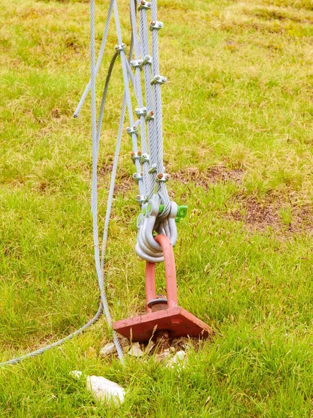 Detail of strong sing and scrap in green yard, iron twisted rope fixed by screws snap hooks and grommets at anchor in ground.