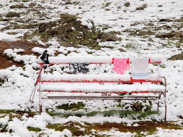 Abandoned red snowy bench with  poles and freeze clothes. Misty morning on the hill in Switzerland Alps. Red wooden bench on meadow, cold snowy and misty weather.