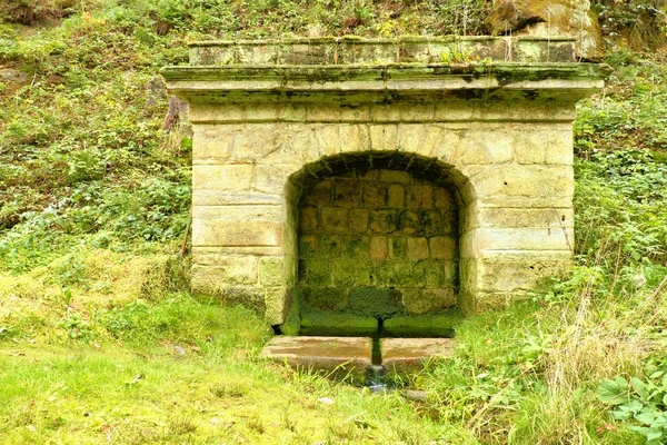Old stony rural fountain in the forest with fresh crystal clear water. . Natural drinking water from mountain stream.