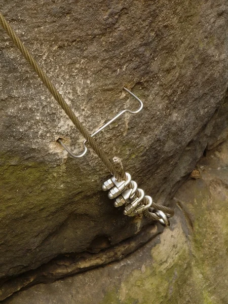Detail of rope end of ferrata way anchored into sandstone rock. Iron twisted rope fixed in block by screws snap hooks.
