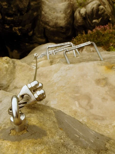 Detail of rope end of ferrata way anchored into sandstone rock. Iron twisted rope fixed in block by screws snap hooks.