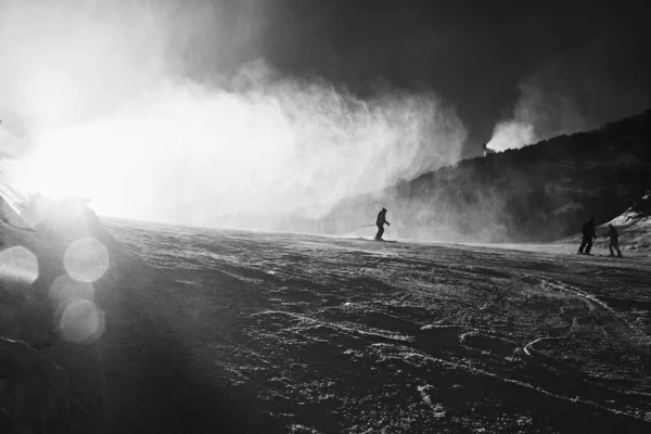 Snow making on slope. Skier near a snow cannon making fresh powder snow. Mountain ski resort and winter calm mountain landscape.