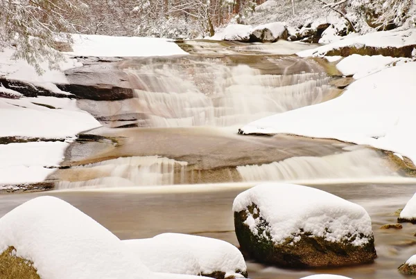 Winter at mountain river. Big stones in stream covered with fresh powder snow and lazy water with low level. Reflections of forest in water level.