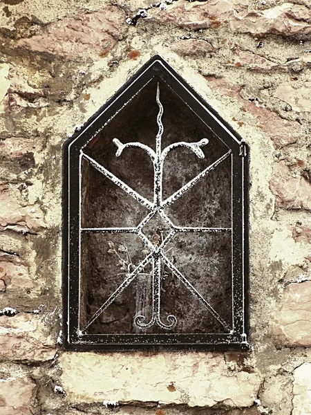 Niche in stony wall of village house with frozen flower. Forged steel bars.