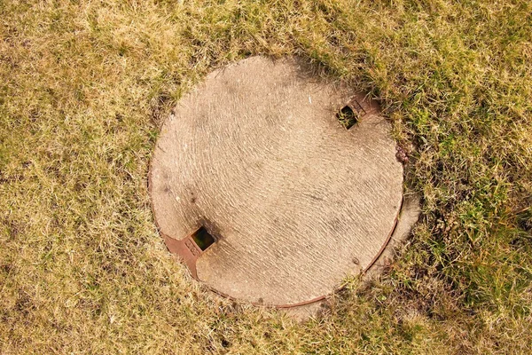 Concrete manhole cover drainage system in the midst of cropped dry grass