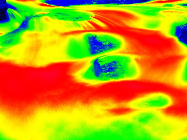 Foamy water level of waterfall, curves between boulders of rapids. Water of mountain river in infrared photo. Amazing thermography.