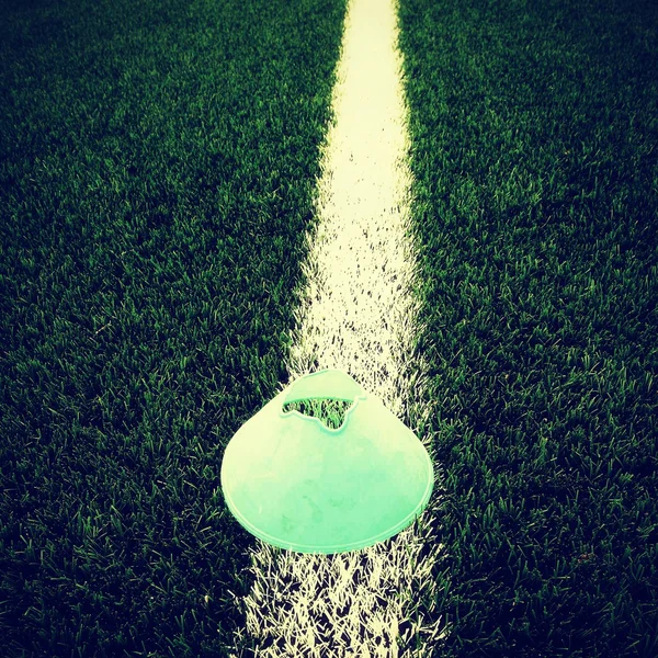 Bright green blue plastic cone on painted white line. Plastic football green turf playground with grind black rubber in core. Dramatic colors.