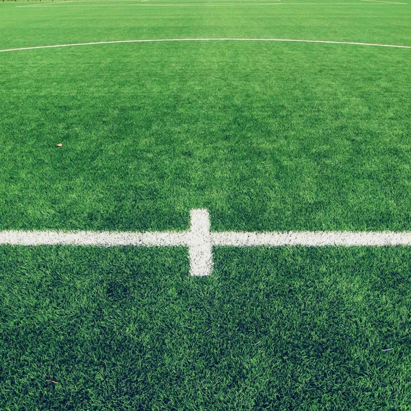 Detail of crossed white lines on outdoor football playground. Detail of lines in a soccer field. Plastic grass and finely ground black rubber.