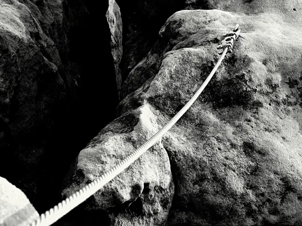 Iron twisted rope streched between rocks in climbers patch.  Rope fixed in block by screws snap hooks. Detail of rope end anchored into sandstone rock