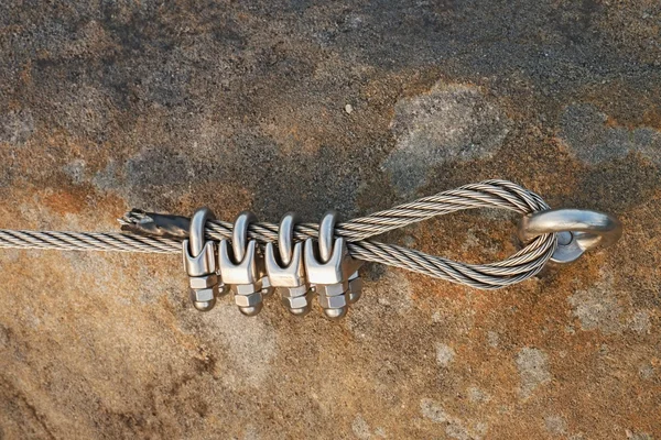 Solid knot on steel rope. Iron twisted rope fixed in block by screws snap hooks. Detail of rope end anchored into sandstone rock