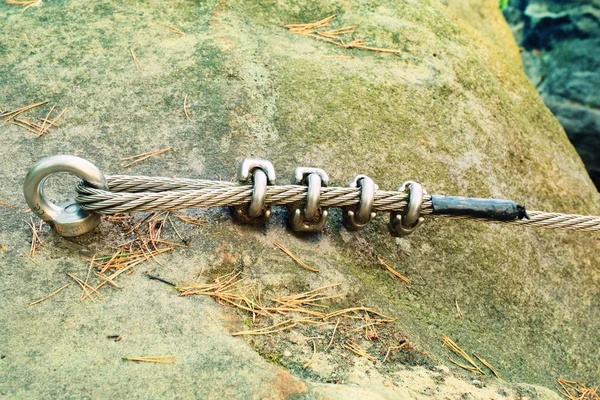 Mountain wall with carabine in the sandstone rock. End of the steel rope in loop.