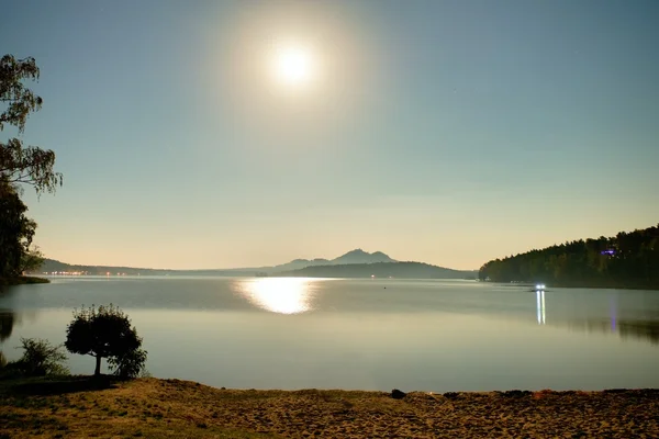 Romantic full moon night at lake, calm water level with moon rays. Burh on the hill.