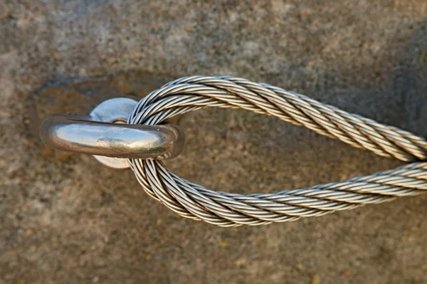 Detail of steel bolt anchor eye in rock. The end knot  of steel rope. Climbers path in rocks via ferrata. Iron twisted rope fixed in block.