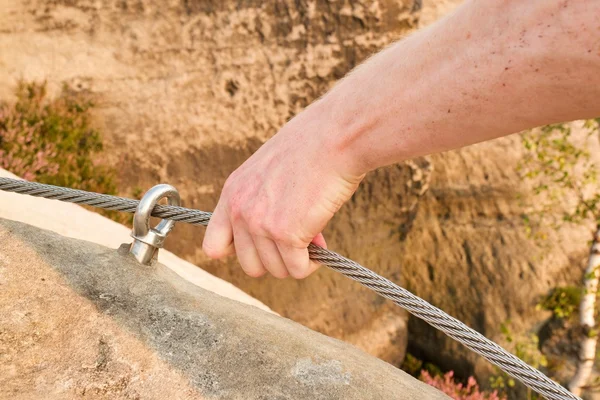 Rock climber\'s hands hold on steel twisted rope at steel bolt eye anchored in rock. Tourist path via ferrata.