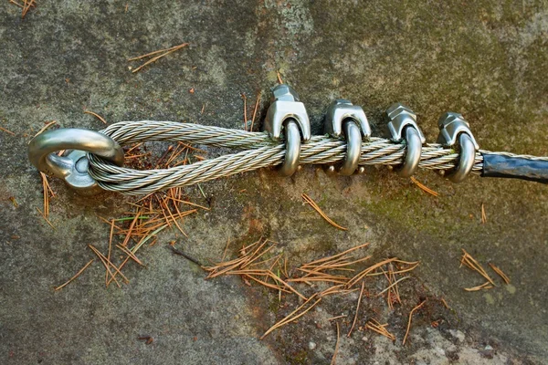 Mountain wall with carabine in the sandstone rock. End of the steel rope in loop.