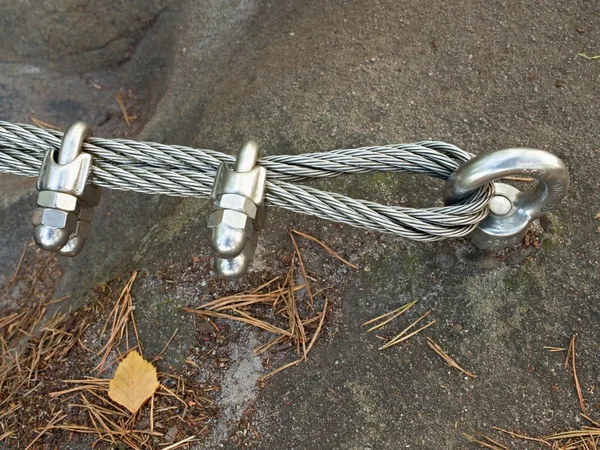 Detail of steel bolt anchor eye in rock. The end knot  of steel rope. Climbers path in rocks via ferrata. Iron twisted rope fixed in block.