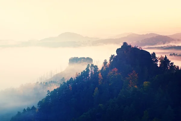 Cold misty daybreak in a fall valley of Bohemian Switzerland park. Hill with hut on the peak increased from magical darkness.