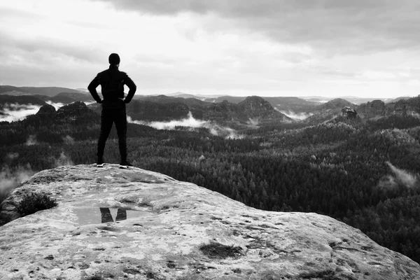 Slim tall tourist on sharp peak of rock in rock empires park is watching over misty and foggy morning valley to Sun