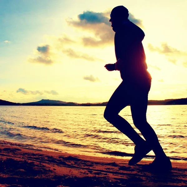 Training at sunset.Running tall man.  A silhouette of jogger at path along lake coastline.