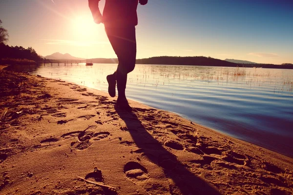 Silhouette of sport active adult man running and exercising on the beach. Calm water, island and sunset sky background.