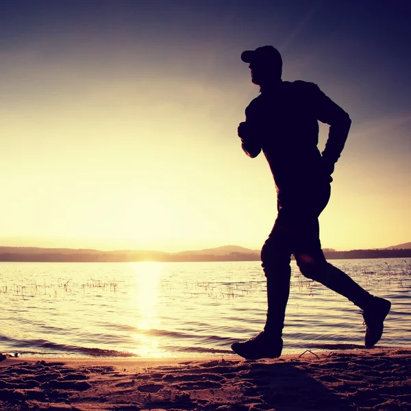 Running man on beach. Sportsman run in baseball cap, jogging guy during the sunrise