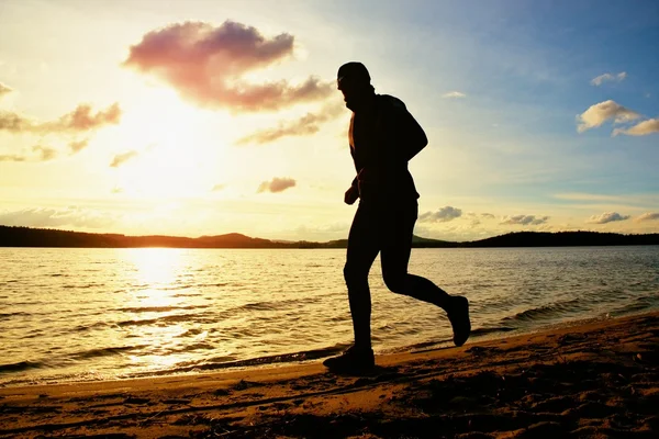 Tall man with sunglasses and dark cap is  running on beach at autumn sunset