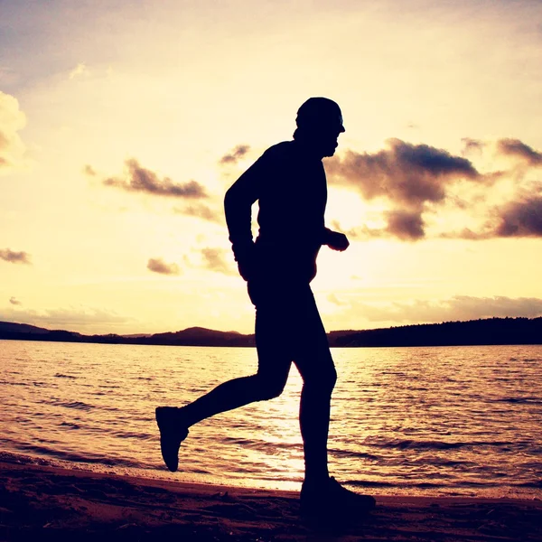 Silhouette of sport active man running and exercising on beach at vivid colorful sunset.