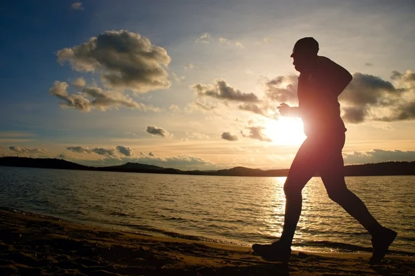 Training at sunset.Running tall man.  A silhouette of jogger at path along lake coastline.