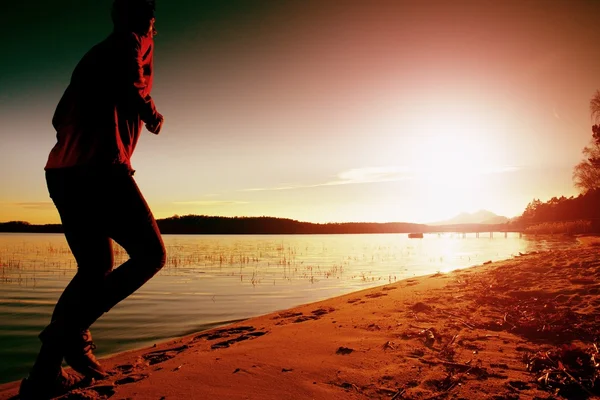 Silhouette of sport active man running and exercising on the beach at sunset.