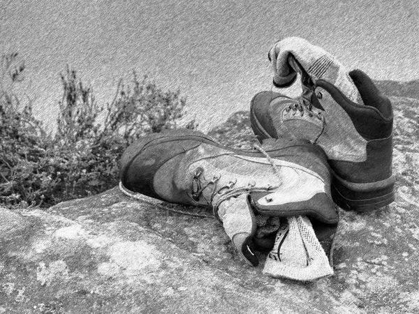 Black and white dashed retro sketch. Hiker high boots and sweaty grey socks. Resting on the boulder at  stream