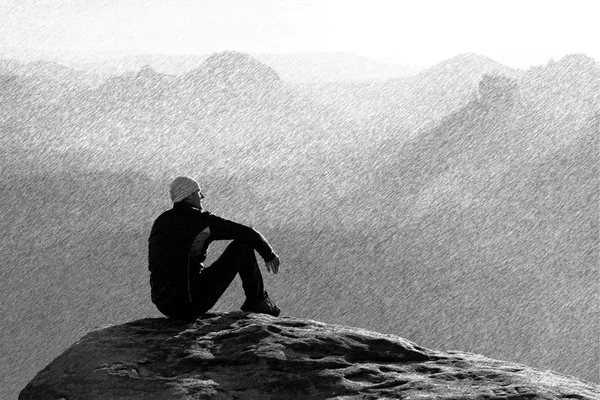 Black and white dashed retro sketch. Moment of loneliness. Man sit on the peak of rock and watching into mist and fog in valley.