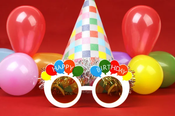 Happy birthday party glasses, party hat and party balloons on red background