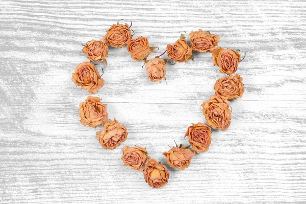 Dry rose flowers heart isolated on white wooden panel