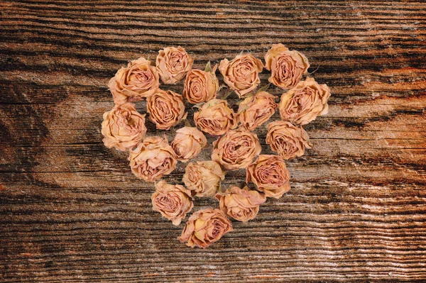 Dry rose flowers heart isolated on wood panel